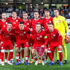 Drużyna piłkarska Polski, w czerwonych strojach, pozuje do zdjęcia. W rękach trzymają flagę z godłem. To dumne polska owcze wyspy!