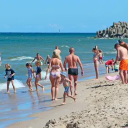 Rodziny na plaży, woda, piasek, falochron. Zastanawiasz się, ile kosztuje nocleg nad morzem?