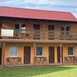 Pomarańczowy budynek z czerwonym dachem, gdzie szukać noclegu. Widać drzwi, okna i balkon.