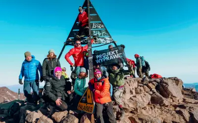 Grupa zdobywców na szczycie Jebel Toubkal podczas trekkingu. Radosna ekipa z flagą "Projekt Wyprawa.pl" cieszy się sukcesem.