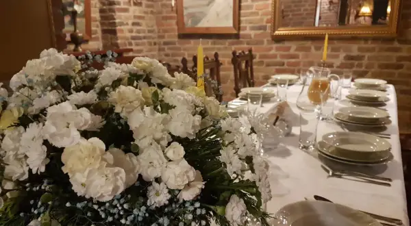 Elegancko nakryty stół z bukietem białych kwiatów i dzbankiem soku. Idealne miejsce, gdzie dobrze zjeść w Nałęczowie.