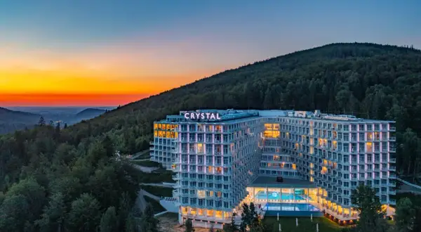 Nowoczesny hotel z widokiem na góry, oświetlony wieczorem, z basenem i tarasami.