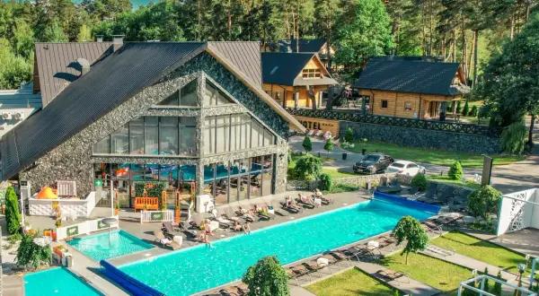 Hotel Bacówka Radawa: basen, leżaki i drewniane domki w otoczeniu lasu.