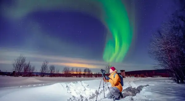 Fotograf uwiecznia zorzę polarną podczas zimowej wyprawy. Zielona poświata tańczy na nocnym niebie nad ośnieżonym krajobrazem.