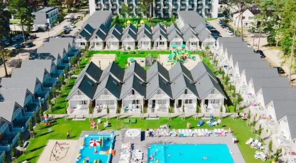 Widok z lotu ptaka na holiday park Kołobrzeg: rzędy białych domków z szarymi dachami, baseny, plac zabaw i zielone tereny.