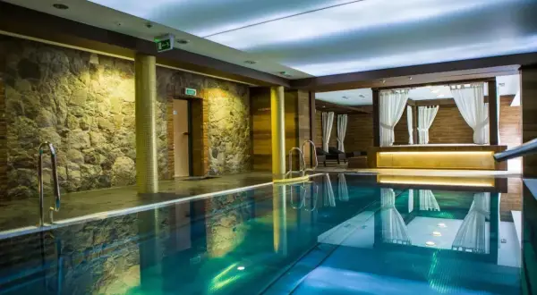 Basen w hotelu Aubrecht Country Spa Resort Koprzywnica. Woda w basenie ma piękny, turkusowy kolor, a ściany zdobi kamień i drewno.