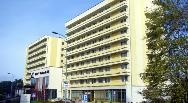 Hotel Vestina w Międzyzdrojach, wysoki, żółty budynek z balkonami, otoczony zielenią.