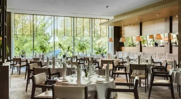 Elegancka sala restauracyjna Grand Hotel Tiffi w Iławie, z widokiem na zieleń. Stoły nakryte do posiłku, gotowe na przyjęcie gości.