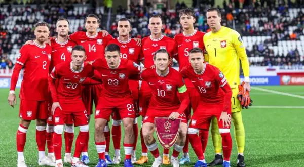 Drużyna piłkarska Polski, w czerwonych strojach, pozuje do zdjęcia. W rękach trzymają flagę z godłem. To dumne polska owcze wyspy!