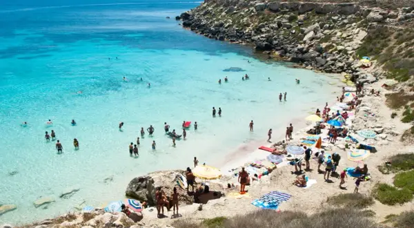 Plaża z turkusową wodą, gdzie jest najcieplejsza woda na świecie. Ludzie kąpią się i opalają na piasku.