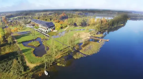Malownicze miejscowości na Mazurach: hotel nad jeziorem, otoczony zielenią i jesiennymi drzewami. Drewniane pomosty zapraszają do wodnych przygód.