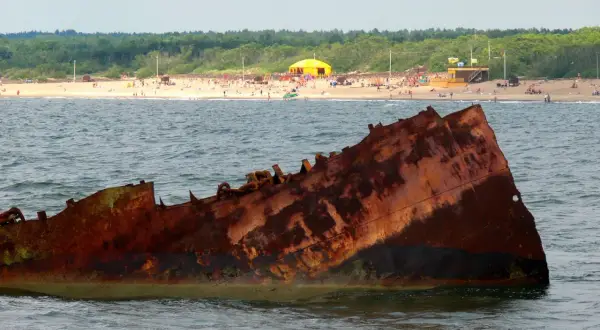 Rdza rdzy, wrak statku na Bałtyku. Czy to symbol, dlaczego wody bałtyku są znacznie zanieczyszczone? W tle plaża z ludźmi.