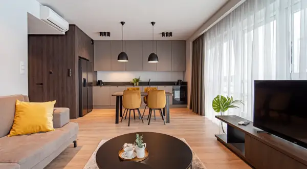 Nowoczesny salon z aneksem kuchennym w hotelu Platinum Residence. Kanapa, stół z krzesłami, kuchnia i TV.