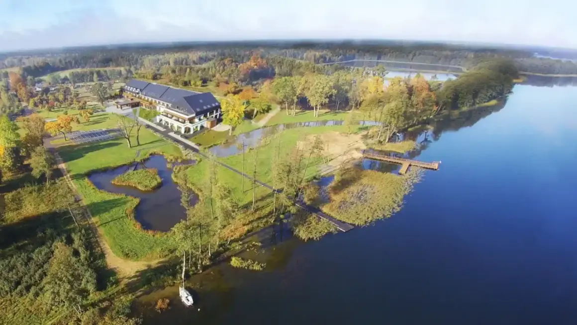 Malownicze miejscowości na Mazurach: hotel nad jeziorem, otoczony zielenią i jesiennymi drzewami. Drewniane pomosty zapraszają do wodnych przygód.