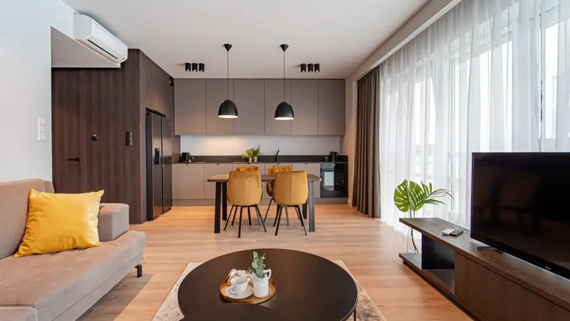 Nowoczesny salon z aneksem kuchennym w hotelu Platinum Residence. Kanapa, stół z krzesłami, kuchnia i TV.