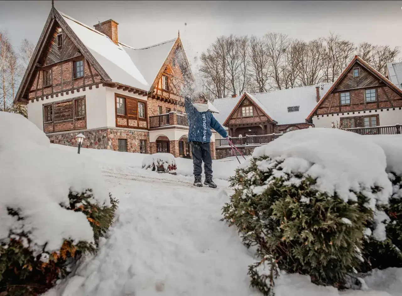 Zimowy dzień w hotelu Aubrecht Country Spa Resort Koprzywnica. Dziecko rzuca śnieżkami przed urokliwym budynkiem.