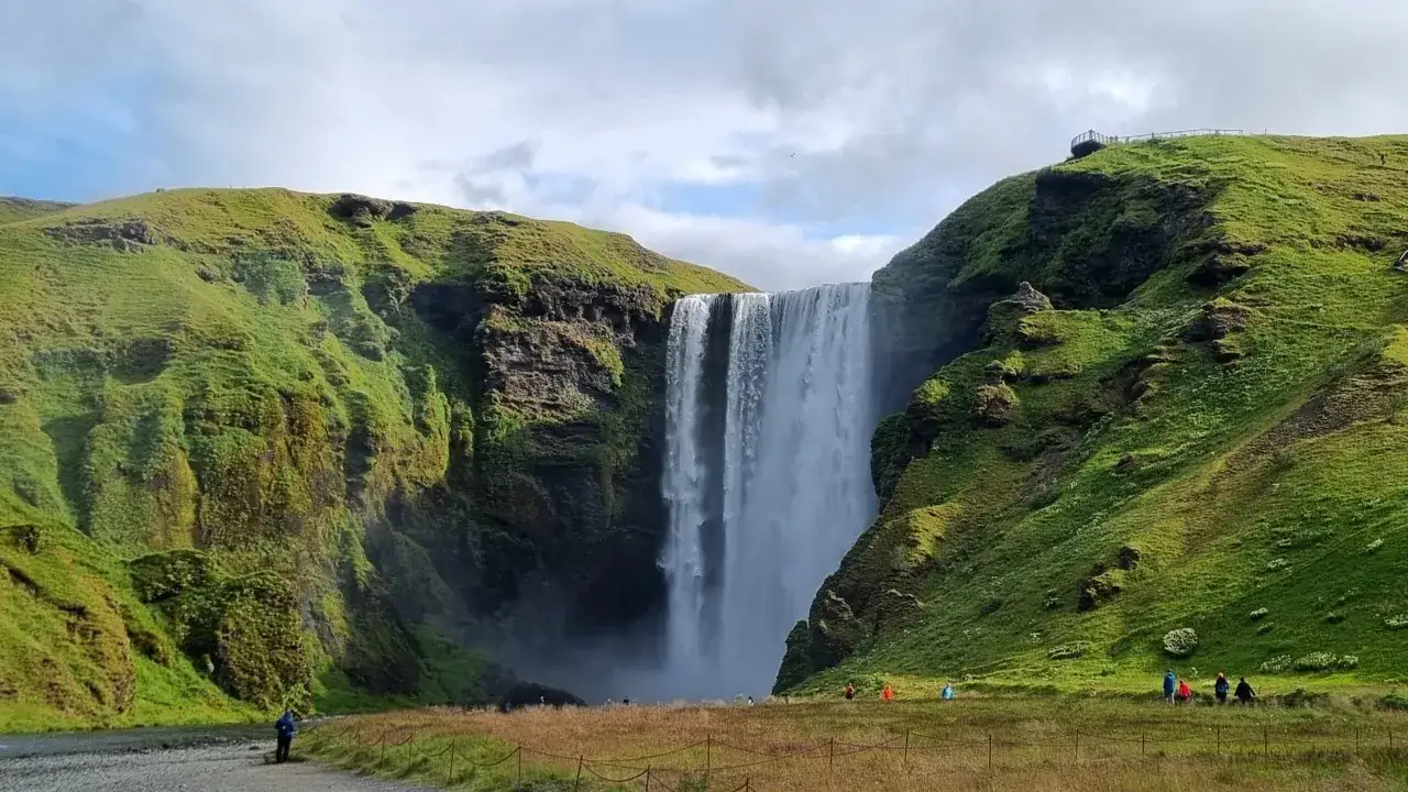 Majestatyczny wodospad Skógafoss na Islandii. W oddali widać małą postać, być może dziecko, podziwiające piękno natury.