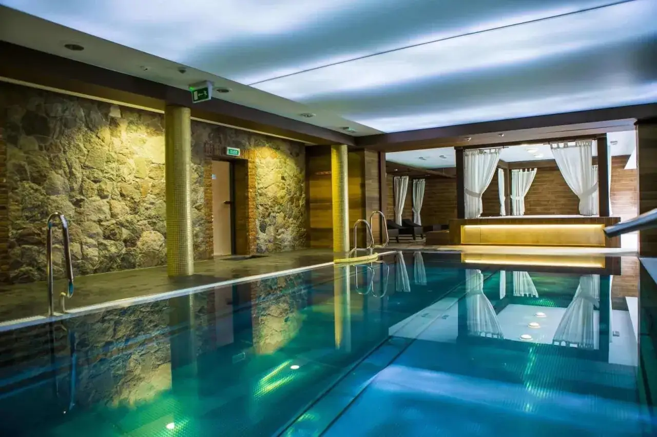 Basen w hotelu Aubrecht Country Spa Resort Koprzywnica. Woda w basenie jest turkusowa, a ściany zdobi kamień i drewno.