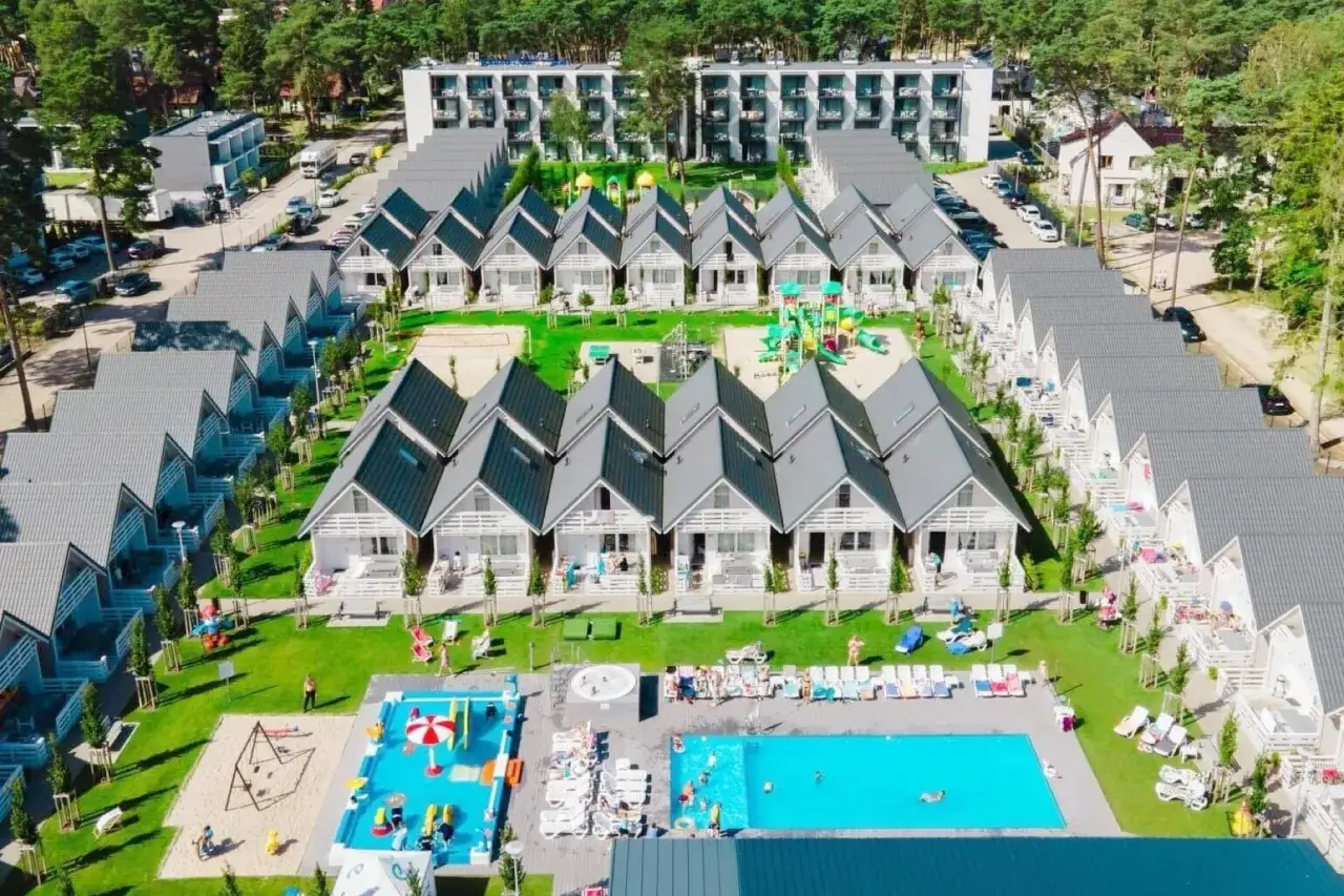 Nowoczesny holiday park Kołobrzeg z białymi domkami, basenem, placem zabaw i zielonym ogrodem.
