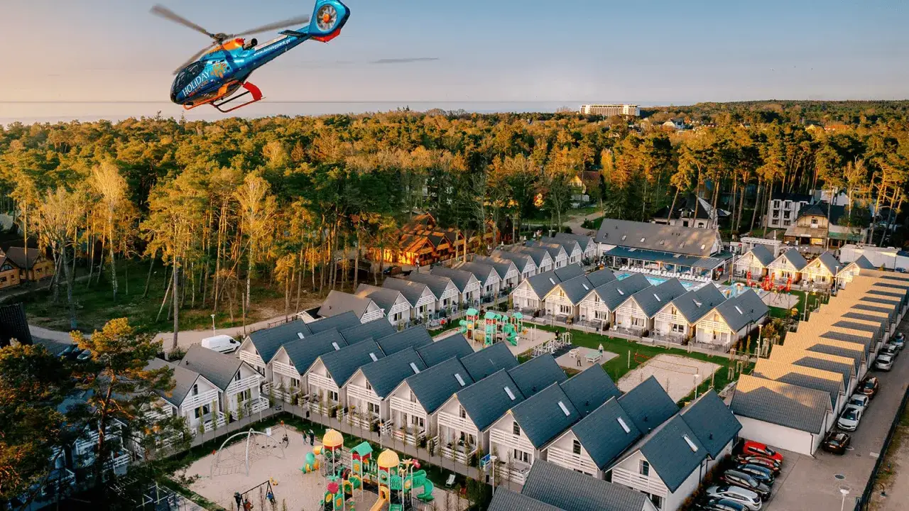 Widok z lotu ptaka na holiday park Kołobrzeg z domkami, basenem i placem zabaw. W tle las i morze.