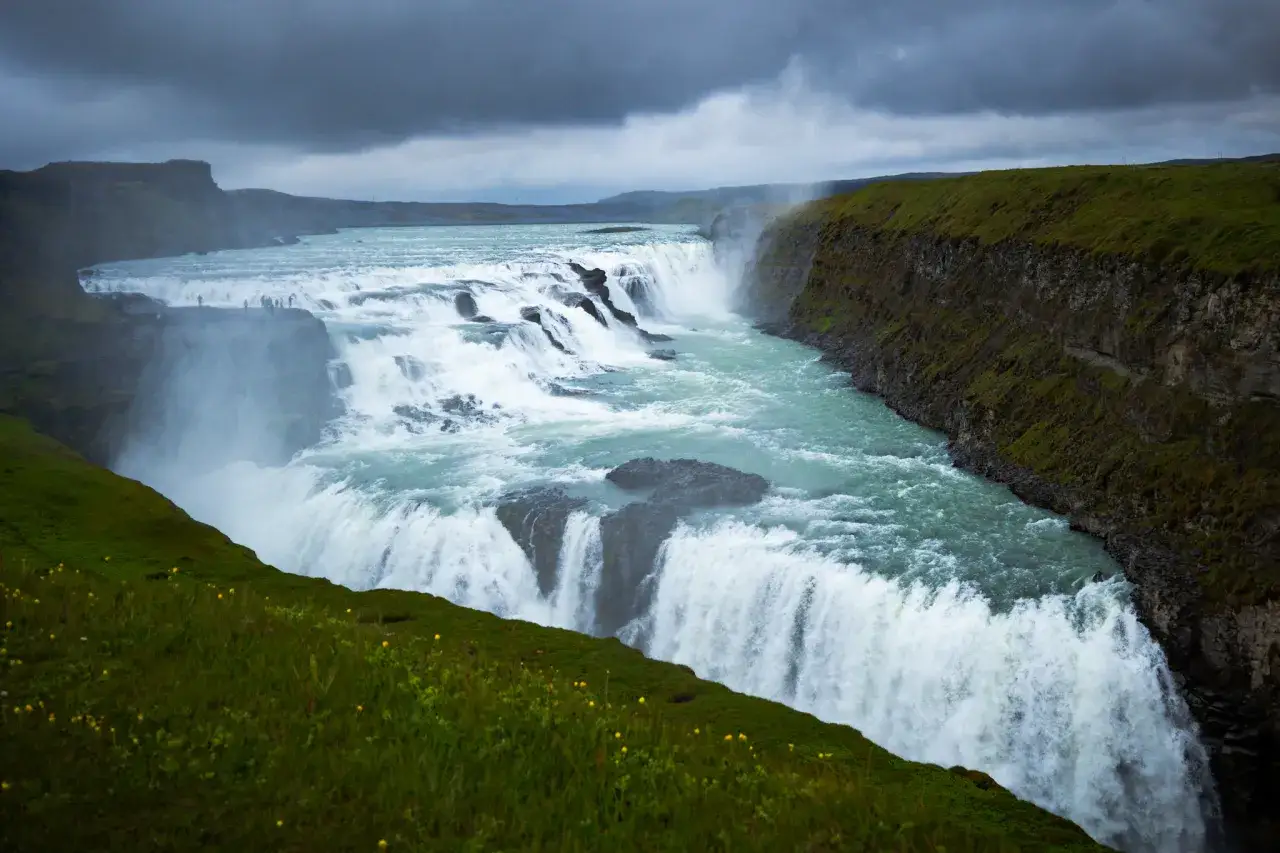 Potężny wodospad Gullfoss, cel wycieczki do Islandii, w otoczeniu zielonych wzgórz i mgły.