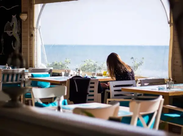 Kobieta siedzi przy stoliku w restauracji z widokiem na morze. Idealne miejsce, gdzie zjeść we Władysławowie.